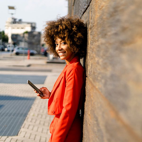 Woman standing next to a wall, holding her phone